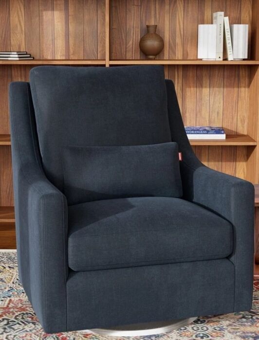 A dark blue armchair with a matching cushion sits on a patterned rug in front of wooden shelves with books, plants, and decorative items.