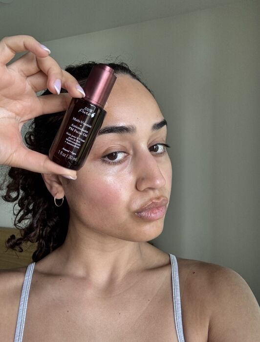 A person holds a bottle of Kiehl’s Midnight Recovery Concentrate close to their face, showing glowing skin in a well-lit room.