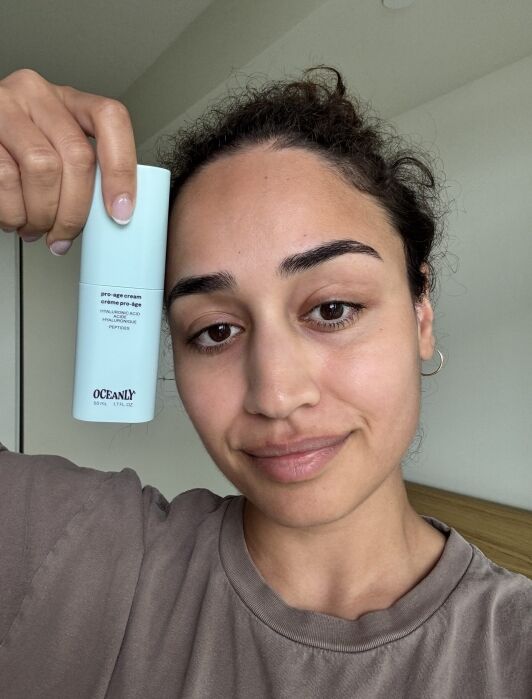 A person holds a light blue Oceanly skincare product next to their face, looking at the camera with a neutral expression.