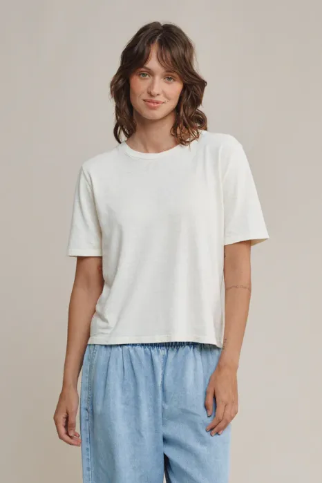 Person standing against a neutral background wearing a plain white t-shirt and light blue pants, looking at the camera with a slight smile.