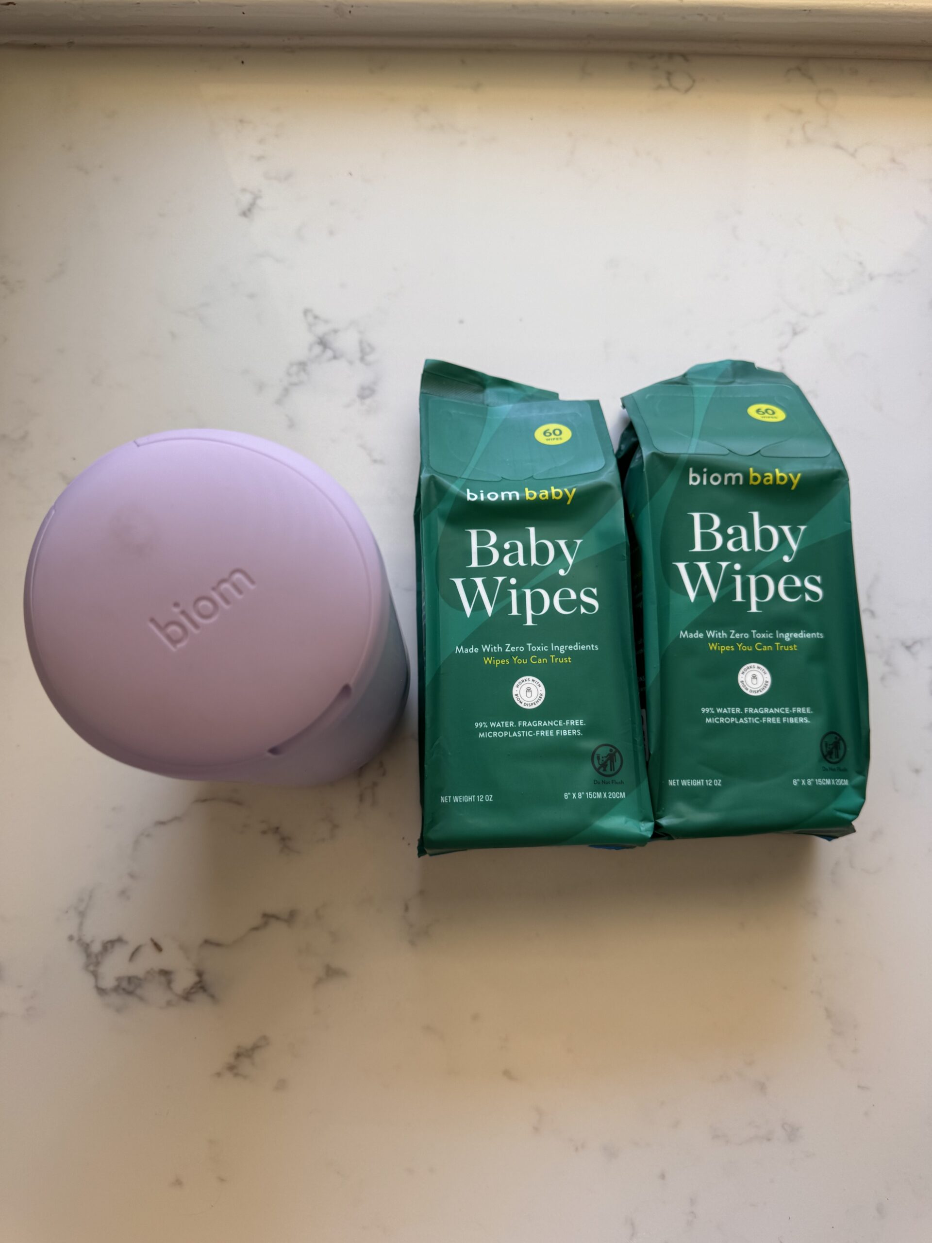 A lavender biom case and two packs of biom baby wipes are placed on a white marble surface.
