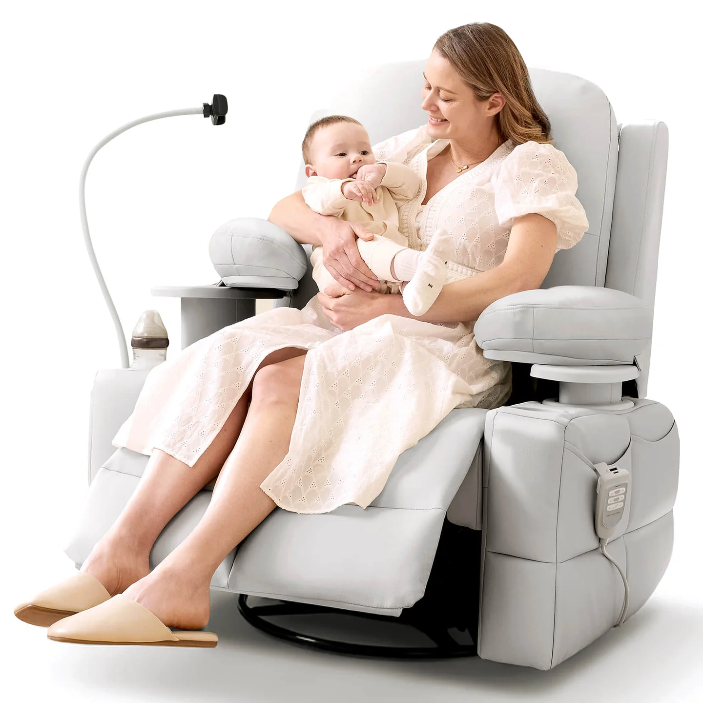 Woman in a white dress sits on a light gray recliner chair, holding a baby. The chair has a bottle holder, side pockets, and an attached reading light.