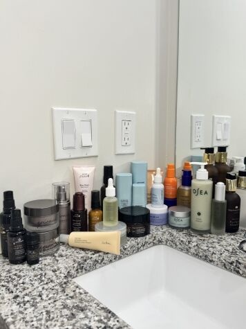 A variety of skincare and beauty products are arranged on a granite bathroom countertop next to a sink and mirror.