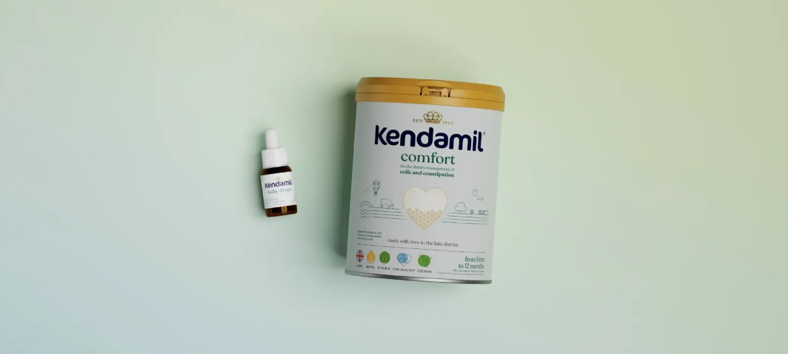 A small dropper bottle and a large tin labeled “Kendamil Comfort” infant formula are placed side by side on a light gradient background.