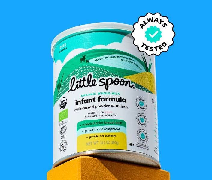 A canister of Little Spoon organic whole milk infant formula is displayed on a yellow block, with an “Always Tested” badge on a solid blue background.