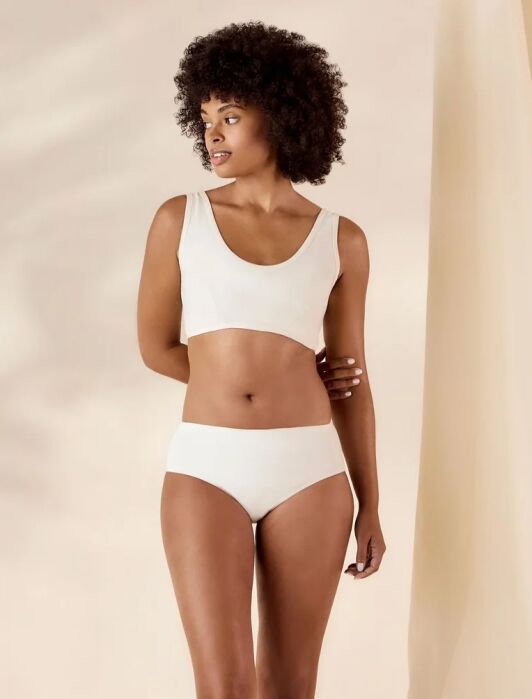 Woman stands wearing a beige bra and matching underwear, looking to the side, against a neutral background.