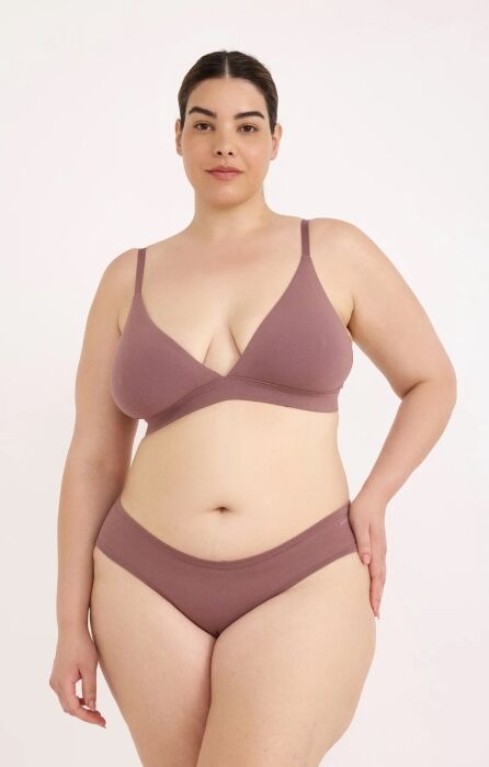 A woman stands against a plain background wearing a matching mauve bra and underwear set, looking directly at the camera with a neutral expression.