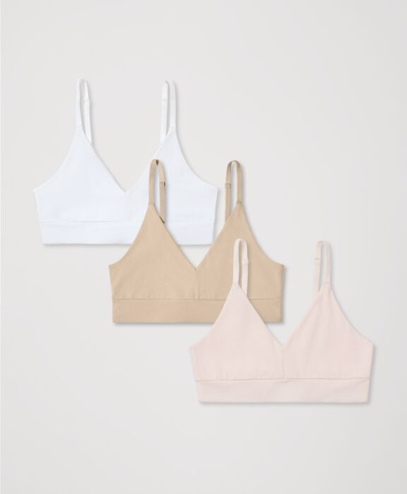Three wireless bralettes in white, beige, and light pink are laid flat on a light background, arranged in a staggered row.