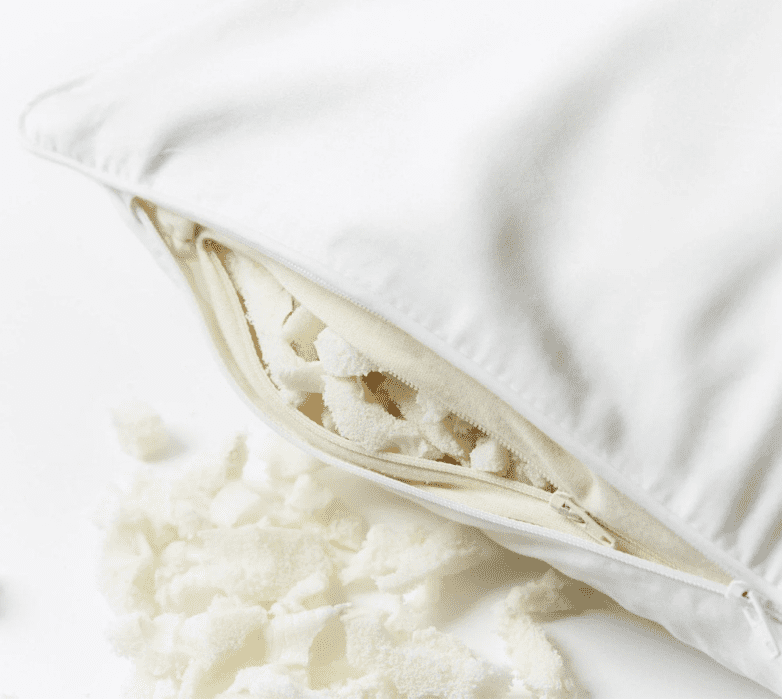 A white pillow with its cover unzipped, showing shredded foam filling inside and some foam pieces scattered outside.