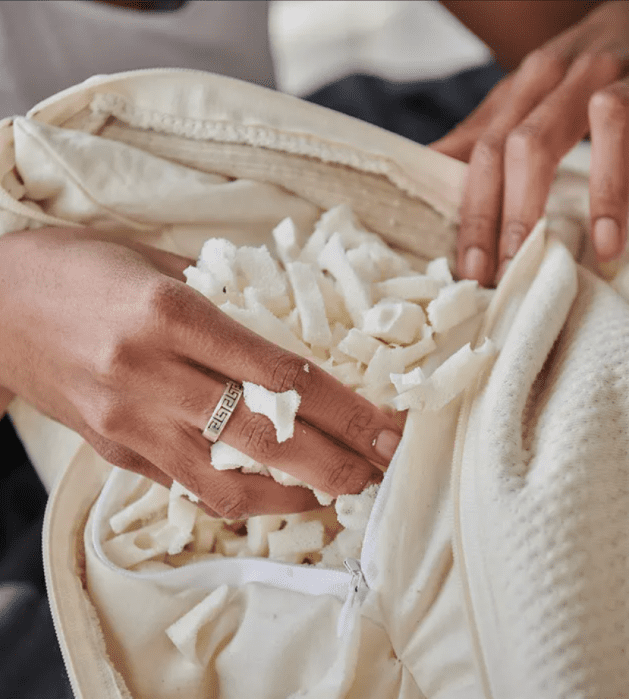 A person’s hands are adjusting and touching shredded white memory foam filling inside an open pillow case.