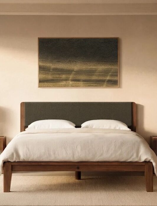 Minimalist bedroom with a neatly made bed, two nightstands with lamps, a dresser with a vase, and a landscape painting above the headboard. Light streams in from a large window.