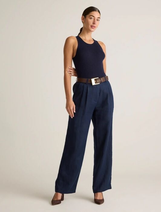 Person wearing a navy sleeveless top, navy wide-leg trousers, brown belt with gold buckle, and brown heels, standing against a plain light background.