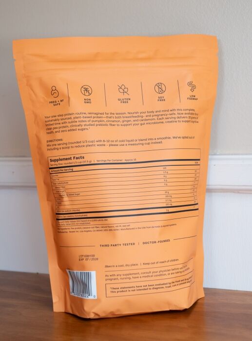Orange resealable pouch of protein powder shown from the back, displaying nutrition facts, ingredients, usage directions, and icons for dietary features like gluten-free and non-GMO.