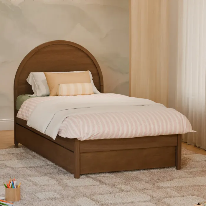 A wooden single bed with light bedding and pillows sits on a beige carpet in a softly lit room with a painted wall and a cup holding colored pencils on the floor.