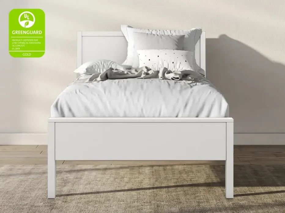 White twin bed with white and gray bedding, set against a beige wall on a wooden floor with a beige rug. GREENGUARD Gold certification badge is visible in the top left corner.