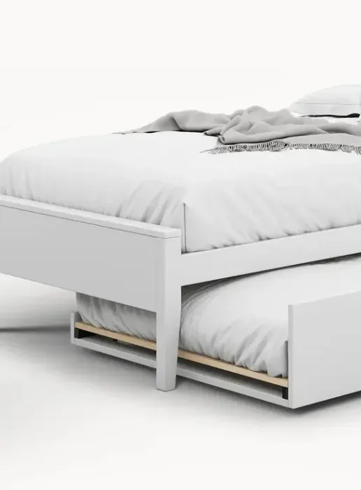 White wooden bed with white bedding and pillows, featuring a pull-out trundle bed underneath. Text reads “Trundle add on available.”.