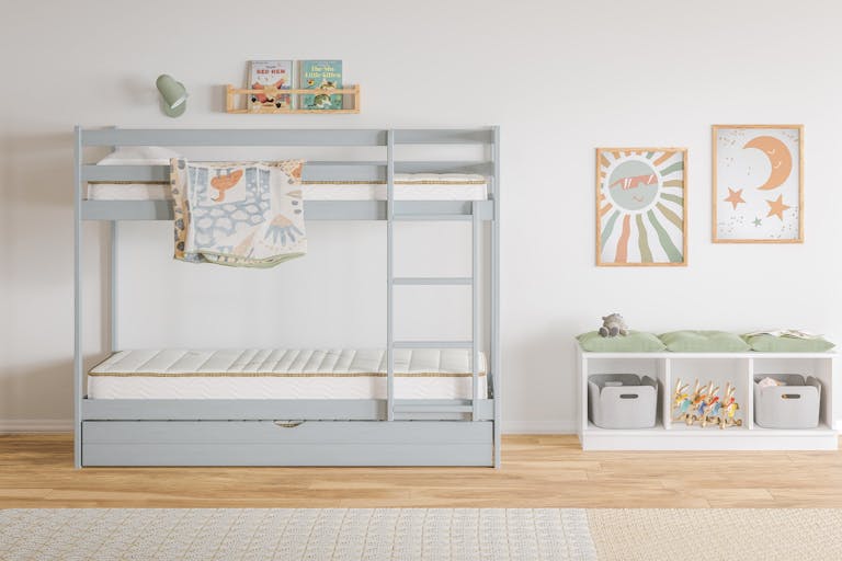 Children’s bedroom with a light gray bunk bed, books and a lamp above, and a storage bench with bins and toys. Two colorful prints decorate the white wall.