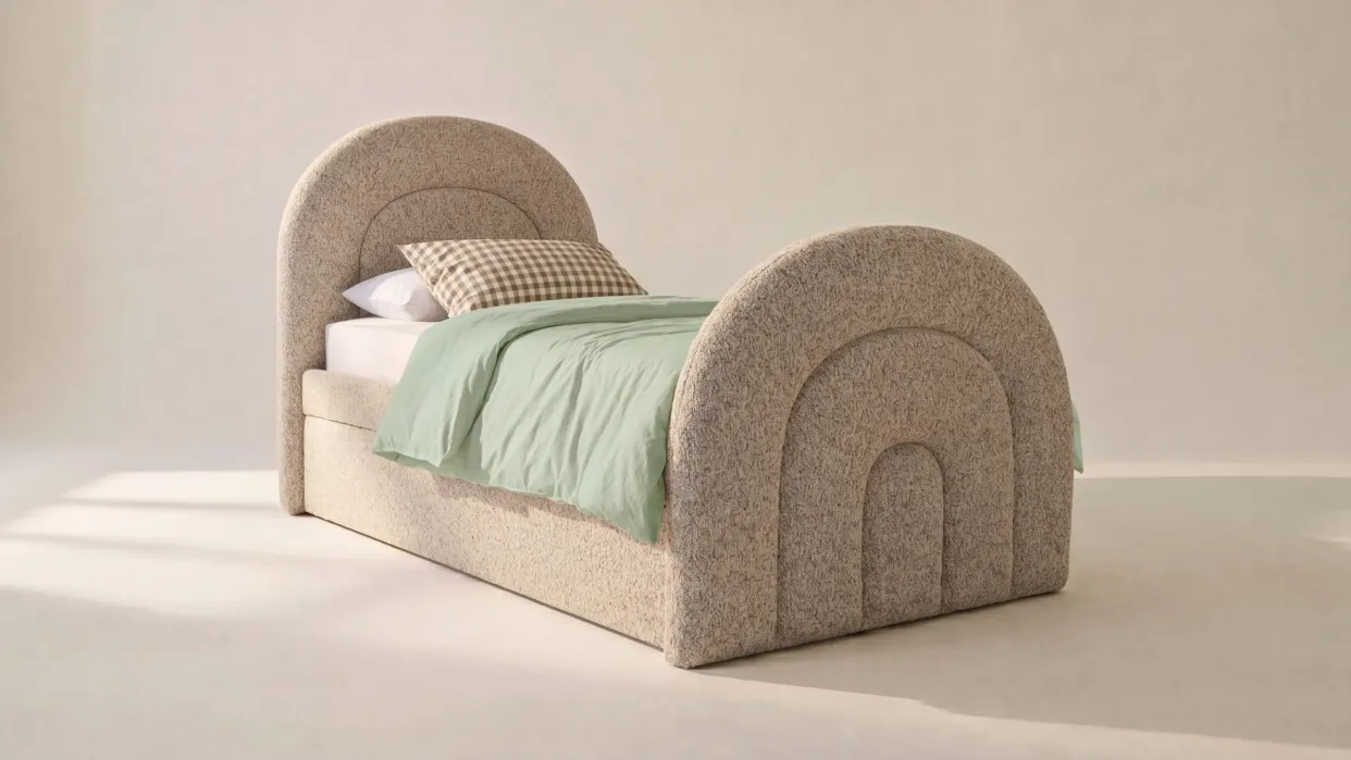 Upholstered twin bed with arched headboard and footboard, green duvet, white sheet, and a checkered pillow on a light-colored background.