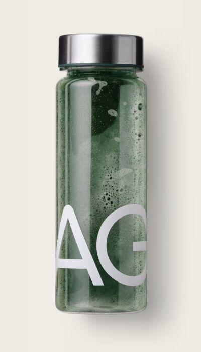 Clear bottle with a metal lid contains a green liquid and displays large white letters “AG” on its side, set against a plain light background.