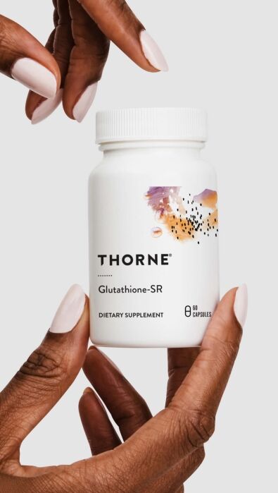 A person holds a white bottle of Thorne Glutathione-SR dietary supplement with 60 capsules, featuring a colorful abstract design on the label.