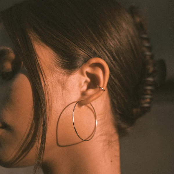 A close-up of a person’s ear wearing a large hoop earring and a small helix piercing, with their hair pulled back in a twisted updo.