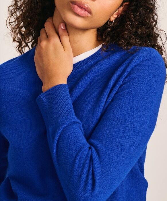 Person wearing a bright blue sweater and small hoop earring, touching their neck with one hand, face partially visible, with curly hair.