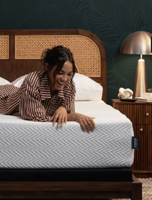 A woman in striped pajamas lies on her stomach on a bed with a patterned white mattress in a modern bedroom with wooden furniture and a gold lamp.