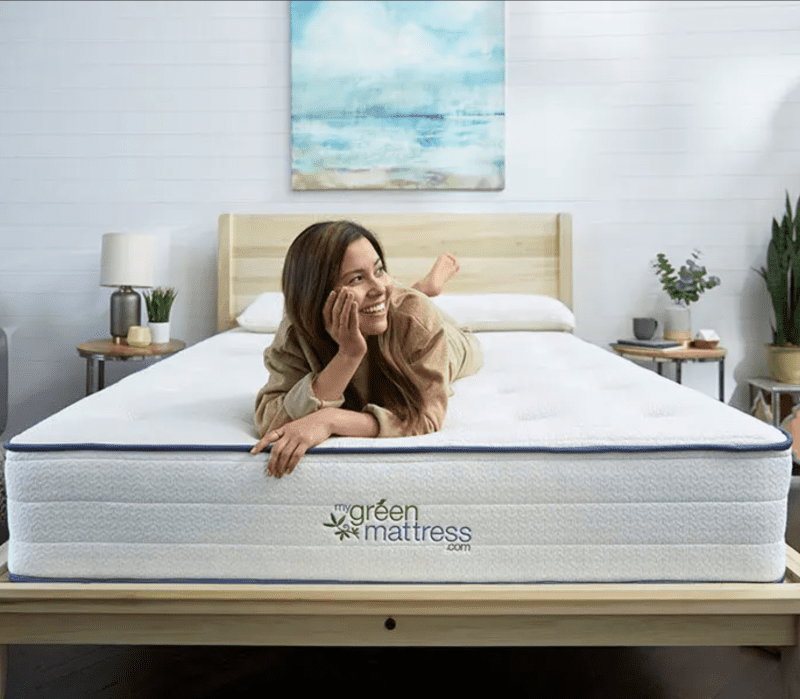 A person lies on a bed with “My Green Mattress” branding in a modern, well-lit bedroom with plants and neutral decor.