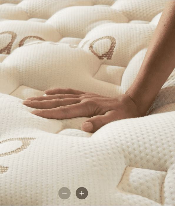 A person presses their hand into the surface of a beige, quilted mattress, demonstrating its softness and texture.