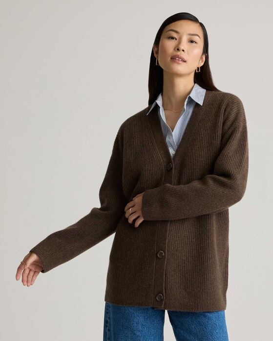 Woman wearing a brown button-up cardigan over a collared shirt and blue jeans, standing against a plain background.