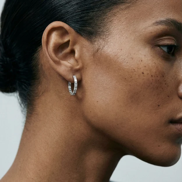 Close-up of a person’s face in profile, showing their ear adorned with a silver hoop earring against a plain background.