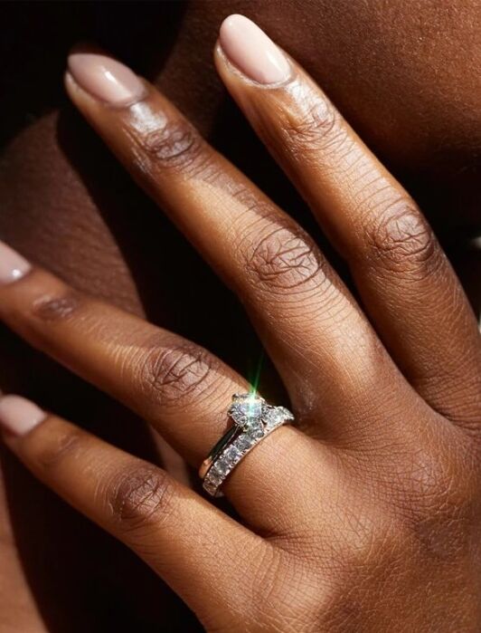 A close-up of a hand wearing a diamond engagement ring set against a blurred background. Text at the bottom reads "Shown with 1.50ct.