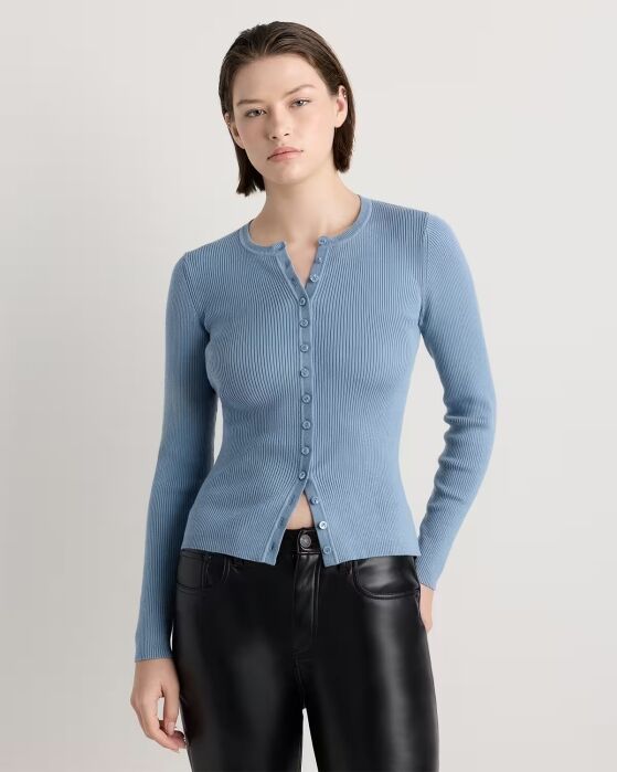 Woman wearing a light blue, ribbed, long-sleeve button-up top and black leather pants, standing against a plain light background.