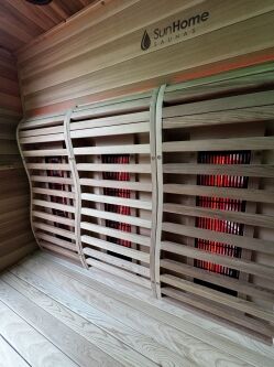 Interior of a wooden infrared sauna with slatted bench and red heating panels, branded "SunHome Saunas" on the upper wall.