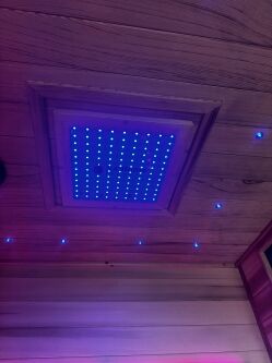 A wooden ceiling with a square panel of blue LED lights in the center and small blue lights installed around it.