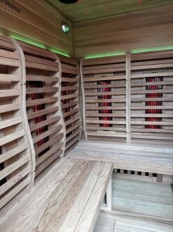 Wooden interior of a modern sauna with curved slatted benches, red heating panels, and green ambient lighting along the walls.