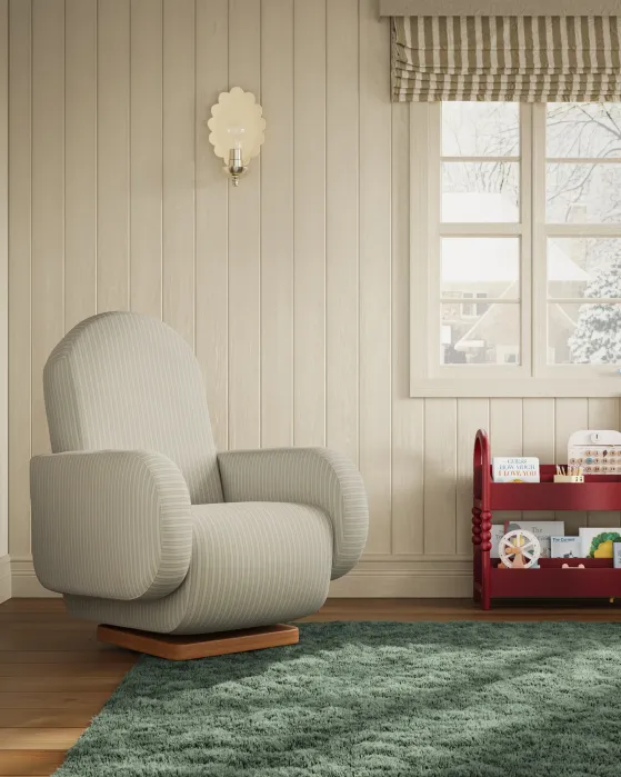 A cozy, striped upholstered armchair sits beside a red bookshelf with children's toys in a light wood-paneled room, featuring a green rug and a window with a snowy outdoor view.