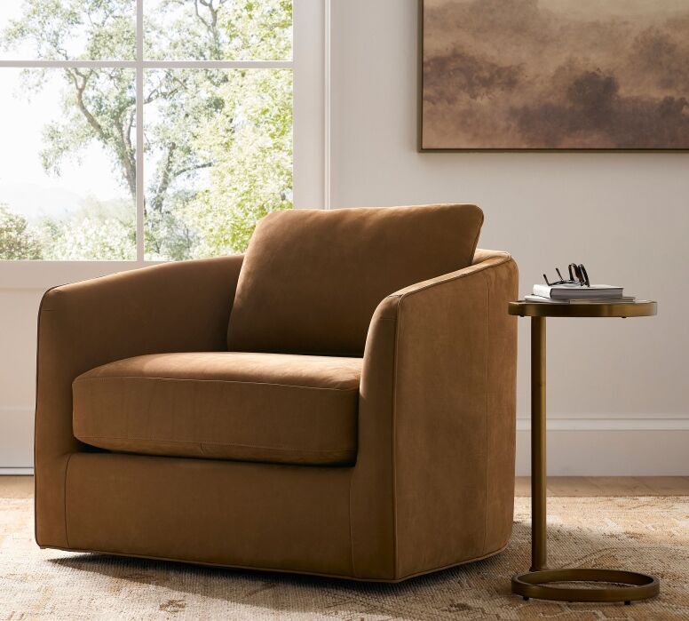 A brown armchair sits next to a small round side table with glasses and a book, positioned by a window with trees visible outside.