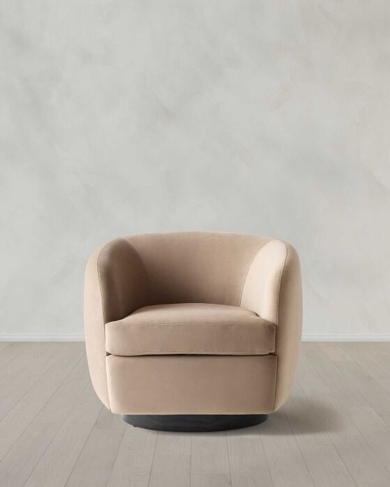 A beige upholstered swivel armchair sits on a light wood floor against a plain, light gray wall.