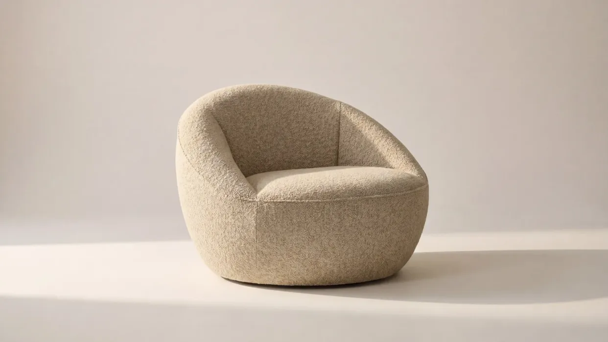 A modern, beige, rounded armchair with a low back and textured upholstery, placed on a light background.