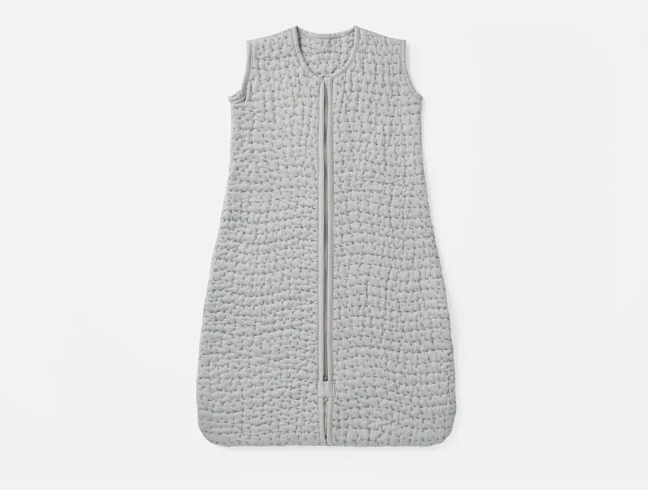 A sleeveless, quilted gray wearable blanket with a front zipper, laid flat on a white background.