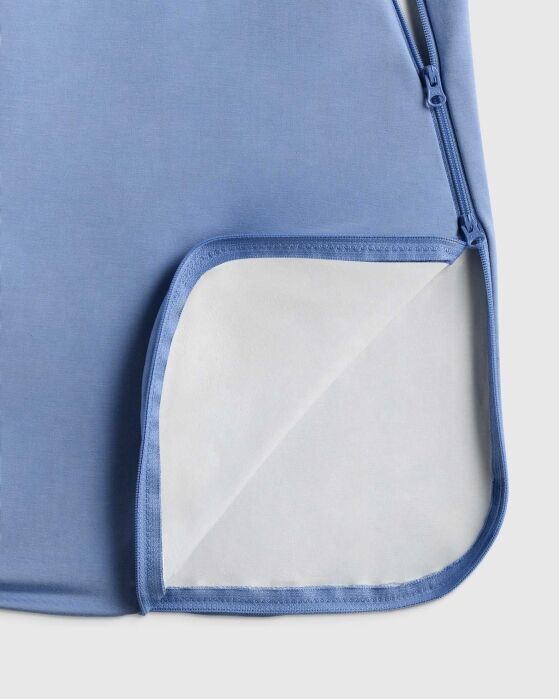 Close-up of a light blue fabric item with a zipper, showing the corner folded back to reveal a white inner lining.