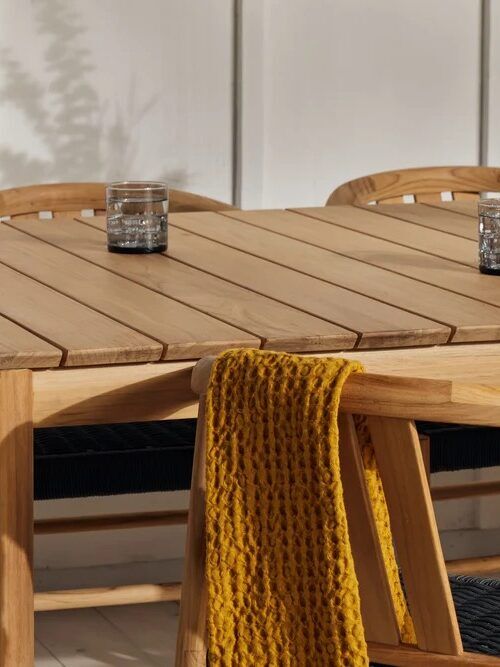 A wooden dining table with two glasses of water, surrounded by chairs; one chair has a yellow knit blanket draped over its back.