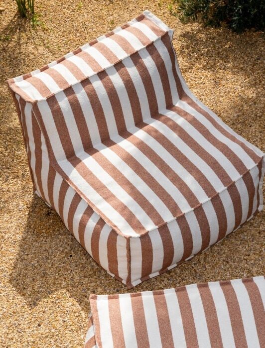 Brown and white striped outdoor bean bag chairs are placed on a gravel surface surrounded by rocks and greenery.