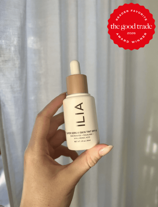 A hand holds a bottle of ILIA Super Serum Skin Tint SPF 40 against a neutral background. A red badge in the corner reads "The Good Trade Reader Favorite Award Winner 2026.