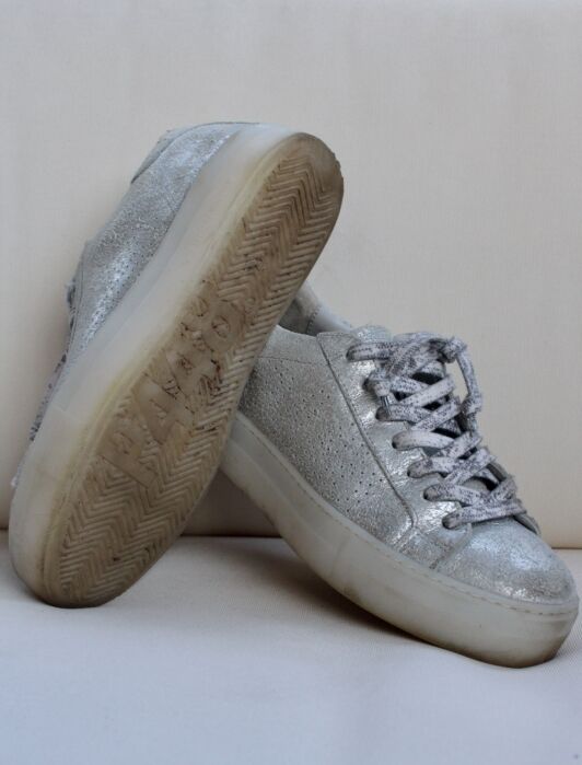 A pair of silver glitter sustainable sneakers with thick white soles, one shoe upright and the other leaning against it, showing worn tread.