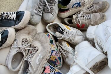 A collection of worn sustainable sneakers and casual styles, featuring various brands and colors, arranged closely together on a light surface.