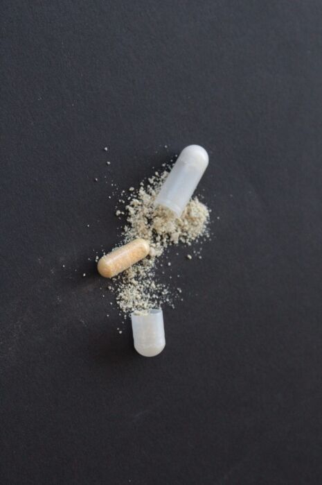Two opened capsules with powder spilling out onto a black surface.