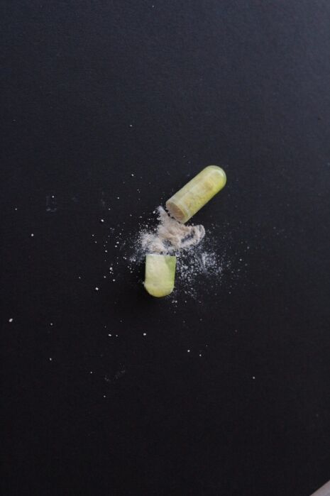 A green capsule pulled apart with white powder spilling out onto a black surface.