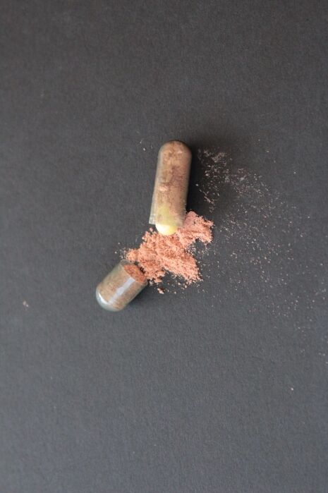 A clear capsule broken open on a black surface, with pink powder spilling out.